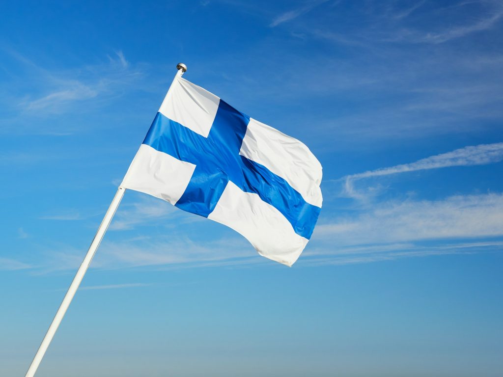 Finnish flag on the flagpole against the blue sky.